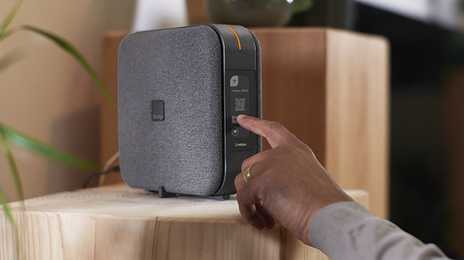 une main touche l'écran tactile de la Livebox 6 Orange pour faire apparaitre le QR code assistance facile